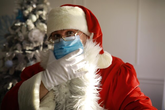 Vrai Père Noël et arbre de Noël sur fond, portant un masque de protection, des lunettes et un chapeau. Noël avec distance sociale. Covid-19