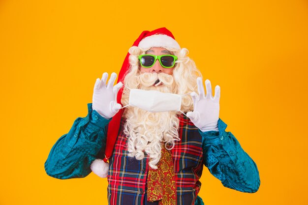 Vrai père Noël sur fond jaune tenant dans les mains un masque de protection contre covid19. Noël avec distance sociale. Covid-19