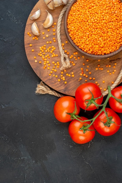 Vue aérienne d'ails de corde de lentilles rouges sur des tomates de planche ronde en bois avec des tiges sur le côté gauche sur fond noir