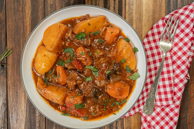 Vue aérienne d'une assiette avec du ragoût de viande, de pommes de terre et de légumes fait maison sur une table en bois