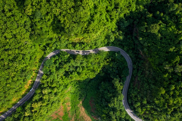 Vue aérienne au-dessus de la forêt de montagne verte pendant la saison des pluies et une route incurvée sur la colline reliant la campagne