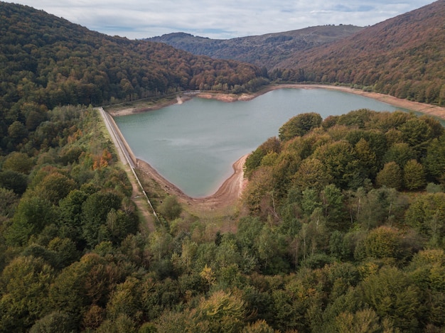 Vue aérienne d'un barrage au coucher du soleil par temps nuageux au milieu d'une forêt montagneuse. Barrage sur une rivière de montagne