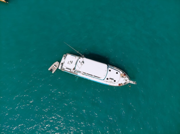 Vue aérienne d'un bateau blanc avec un arc pointu et et un petit bateau à côté de lui naviguant à travers la mer