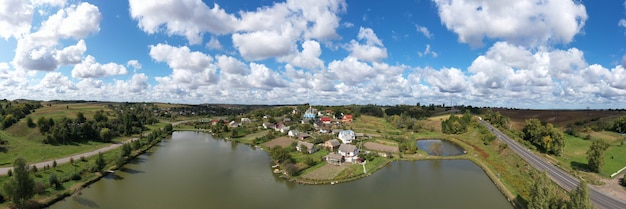 Vue aérienne d'un beau paysage de village sur une colline près du lac. Au centre du village sur une colline se trouve une ancienne belle église. De beaux nuages mystiques et envoûtants coulent sur le village
