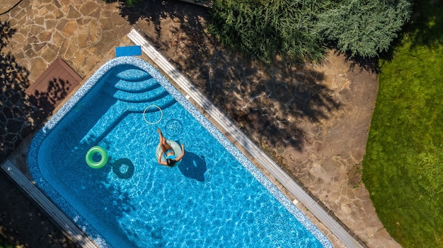 Vue aérienne de la belle fille dans la piscine d'en haut, nager sur un anneau gonflable et s'amuser dans l'eau sur un complexe de vacances tropical