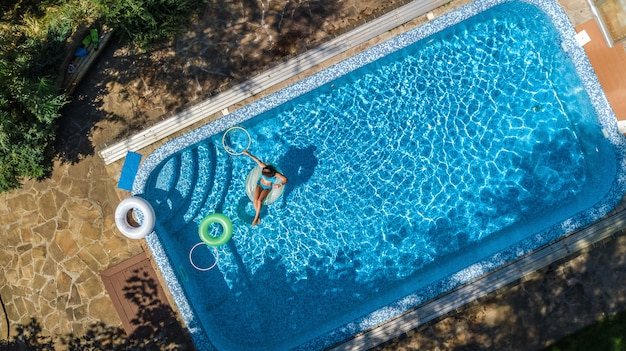 Vue aérienne de la belle fille dans la piscine d'en haut, nager sur l'anneau gonflable et s'amuser dans l'eau en vacances en famille sur tropical resort de vacances