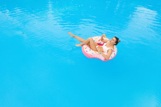 Vue aérienne de la belle jeune fille en bikini blanc reposant sur un beignet gonflable dans la piscine. Fond de vacances d'été