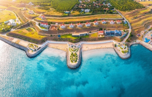 Vue aérienne de la belle plage de sable bleu promenade de la mer abrite des parasols de piscine eau arbres verts sur les collines au coucher du soleil en été Vue de dessus du front de mer et de la ville de chalets Paysage tropical