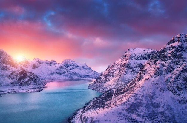 Vue aérienne de belles montagnes enneigées ciel de route de mer avec des nuages roses au coucher du soleil en hiver îles Lofoten Norvège Vue de dessus des rochers dans la neige côte de la mer eau azur Vue d'en haut Nature