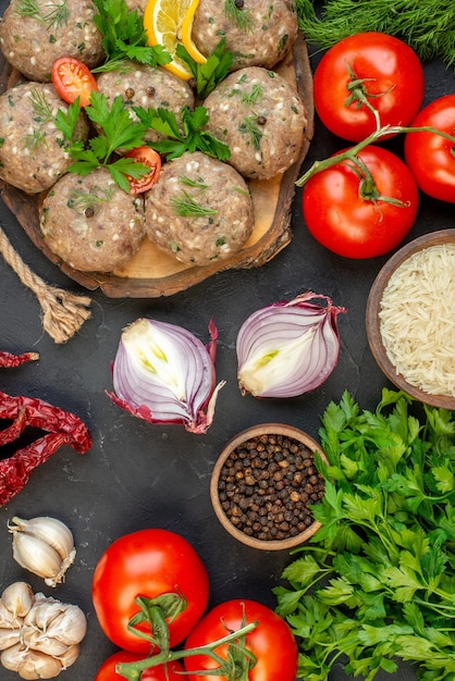 Vue aérienne de boulettes de viande non cuites sur une planche à découper en bois et de légumes frais poivre sel sur fond de vague sombre