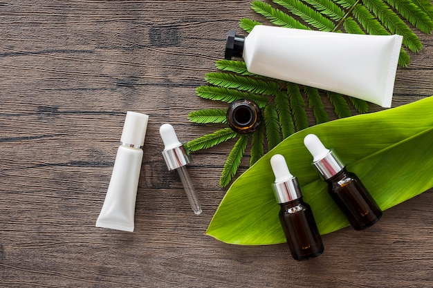 Vue aérienne des bouteilles d&#39;huile essentielle et tube cosmétique blanc sur les feuilles vertes au-dessus de la table en bois