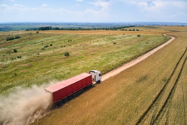 Vue aérienne d'un camion de fret roulant sur un chemin de terre entre des champs de blé agricoles faisant beaucoup de poussière Transport de céréales après avoir été récolté par une moissonneuse-batteuse pendant la saison des récoltes