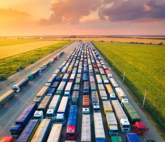 Vue aérienne de camions colorés dans le terminal au coucher du soleil en été Vue de dessus du centre logistique Transport Transport de marchandises Expédition Camionnage international Vue depuis le drone du ciel de la route des camions