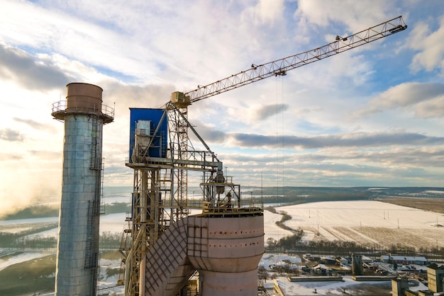 Vue aérienne de la cimenterie avec une structure d'usine élevée et une grue à tour dans la zone de production industrielle au coucher du soleil.