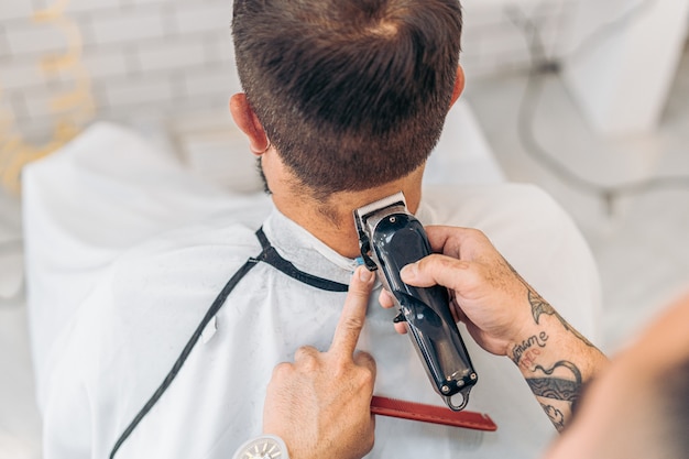 Vue aérienne d'un coiffeur coupant les cheveux d'un homme en robe à l'aide d'une machine électrique dans un salon de coiffure