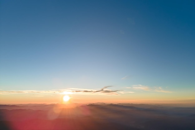 Vue aérienne des collines de montagne sombres avec des rayons de soleil brillants du soleil couchant au coucher du soleil. Pics brumeux et vallées brumeuses le soir