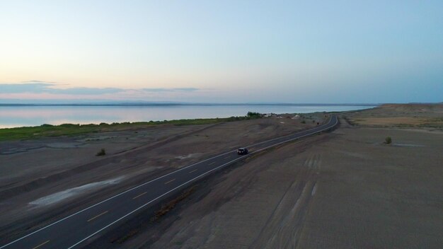 Vue aérienne de la conduite automobile pendant le coucher du soleil sur une route déserte au milieu du désert