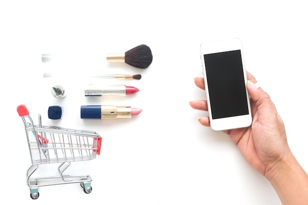 Vue aérienne de cosmétiques et de panier avec une main de femme tenant le téléphone mobile, achats en ligne, vendredi noir