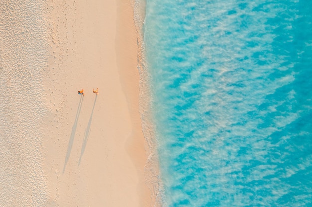 Vue aérienne d'un couple marchant sur la plage avec la lumière du soleil à proximité des vagues de la mer turquoise. Vue de dessus l'été