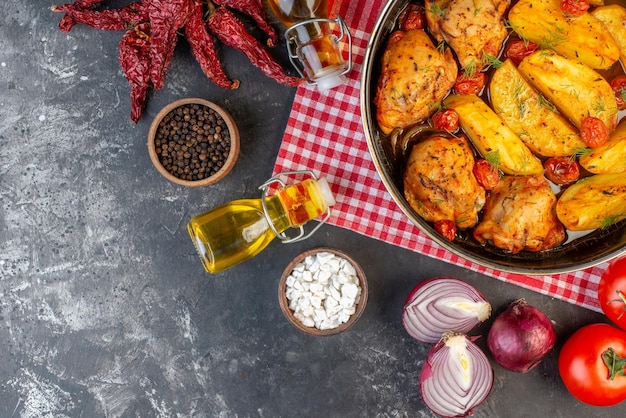 Vue aérienne d'un délicieux dîner avec des poulets pommes de terre verts dans une casserole sur une serviette rouge pliée poivrons séchés bouteilles d'huile tombées légumes