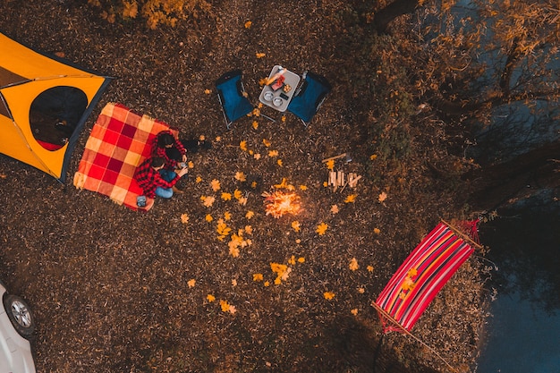 Vue aérienne de dessus du camping d'automne avec feu de joie hamac voiture tente. couple heureux se reposant à l'extérieur