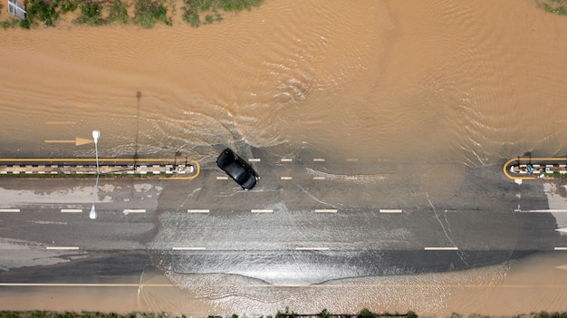 Vue aérienne de dessus du village inondé et de la route de campagne avec voiture, vue d'en haut prise par drone