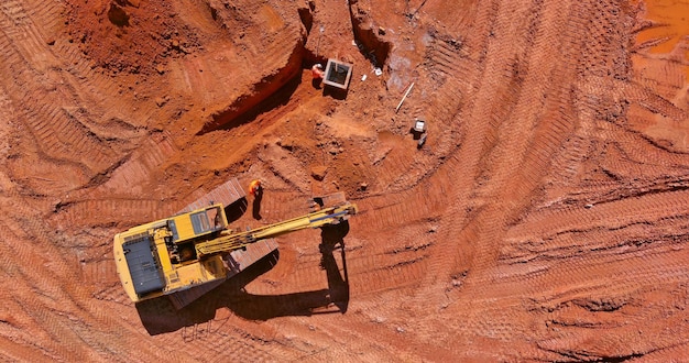 Vue aérienne de dessus de l'excavatrice travaillant à la rétrocaveuse creuse le sol pour la pose de tuyaux en béton sur la construction