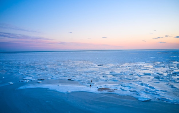 Vue aérienne deux personnes marchent sur la glace au coucher du soleil sur la mer gelée Paysage d'hiver au bord de la mer au crépuscule Vue d'en haut de la fonte des glaces dans l'océan au lever du soleil Réchauffement climatique Horizon coloré vif