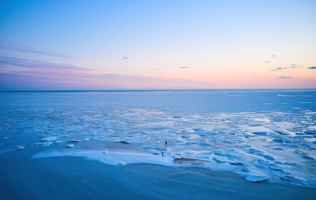 Vue aérienne deux personnes marchent sur la glace au coucher du soleil sur le paysage d'hiver de la mer gelée au bord de la mer pendant