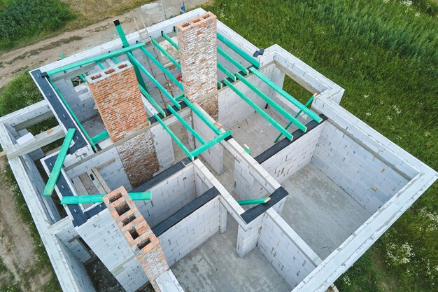 Vue aérienne du cadre inachevé d'une maison privée avec des murs en béton léger aéré et des poutres de toit en bois en construction.