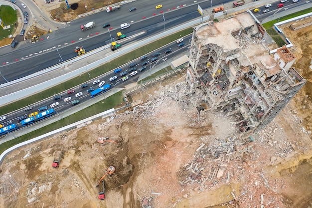 Vue aérienne du chantier de construction avec bâtiment industriel détruit et excavatrices et embouteillage.