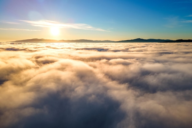 Vue aérienne du coucher de soleil jaune sur des nuages gonflés blancs avec des montagnes lointaines à l'horizon