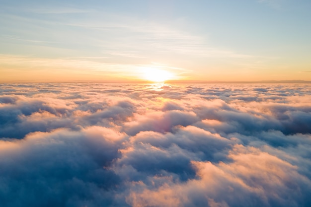 Vue aérienne du coucher de soleil jaune vif sur des nuages denses blancs avec un ciel bleu au-dessus.