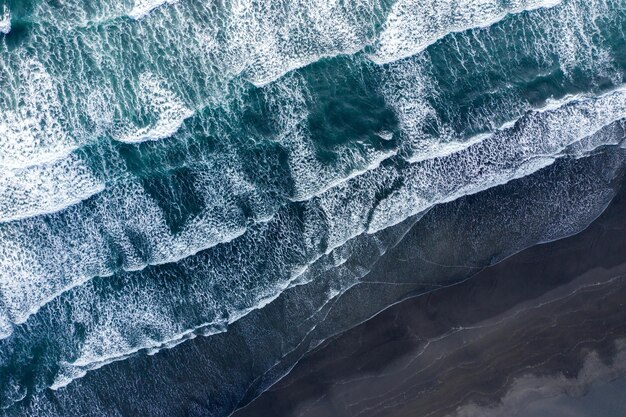 Vue aérienne du drone des vagues de l'océan Atlantique lavant la plage de sable basaltique noir d'Islande