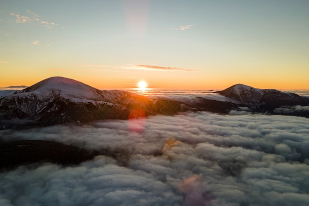 Vue aérienne du lever du soleil vibrant sur un brouillard dense blanc avec des montagnes sombres des Carpates lointaines à l'horizon.