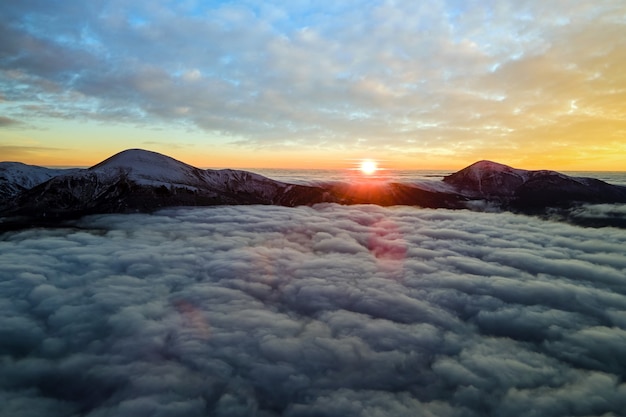 Vue aérienne du lever du soleil vibrant sur un brouillard dense blanc avec des montagnes sombres des Carpates lointaines à l'horizon.