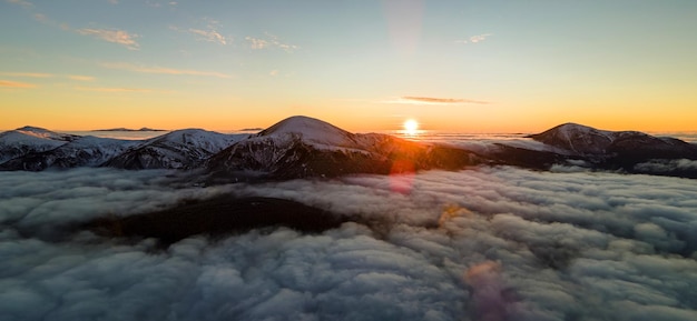 Vue aérienne du lever du soleil vibrant sur des nuages blancs denses avec des montagnes sombres lointaines à l'horizon