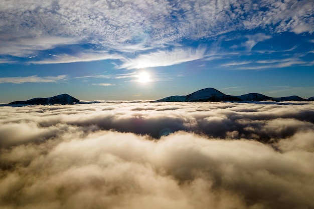 Vue aérienne du lever du soleil vibrant sur des nuages blancs denses avec des montagnes sombres lointaines à l'horizon