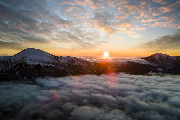 Vue aérienne du lever du soleil vibrant sur des nuages denses blancs avec des montagnes sombres lointaines à l'horizon.