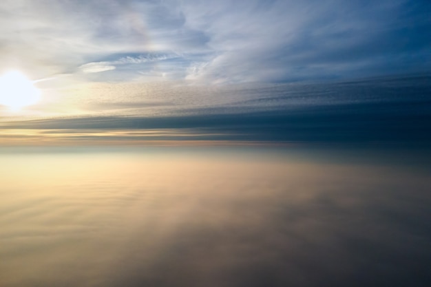 Vue aérienne du lever de soleil jaune vif sur des nuages denses blancs avec un ciel bleu au-dessus.