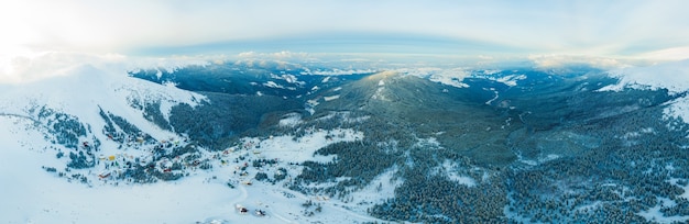 Vue aérienne du magnifique panorama hivernal des pentes enneigées et des collines parmi les nuages blancs luxuriants. Le concept de la nature hivernale envoûtante