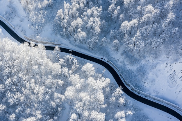 Vue aérienne du paysage d'hiver de la route de montagne sinueuse dans une forêt couverte de neige éclairée par un soleil levant