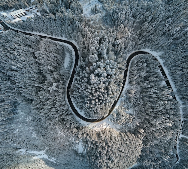 Vue aérienne du paysage hivernal avec des collines de montagne couvertes de neige et une route forestière sinueuse le matin.