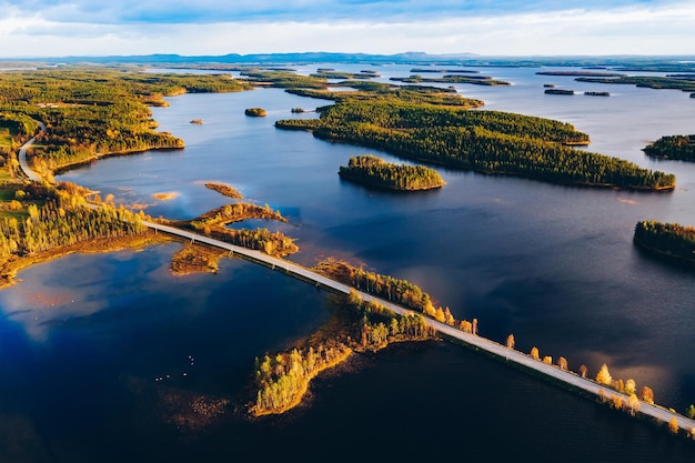 Vue aérienne du pont routier à travers les lacs bleus avec des îles et une forêt d'automne colorée en Laponie finlandaise