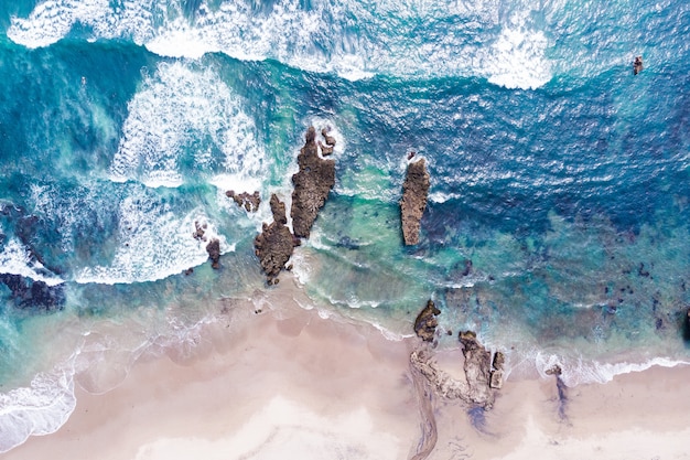 Vue aérienne du rivage de l'océan avec des vagues se brisant sur les rochers et la plage de sable blanc