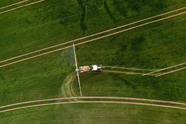 Vue aérienne du tracteur pulvérisant les produits chimiques sur le grand champ vert