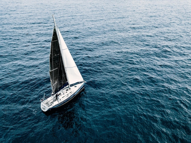 Vue aérienne du yacht de voilier avec des voiles blanches et noires en pleine mer en Italie