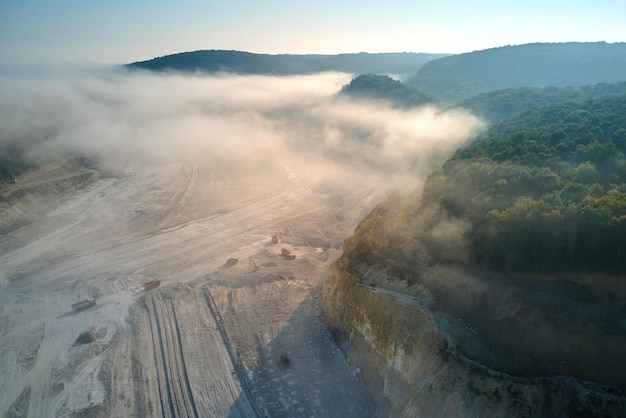 Vue aérienne de l'exploitation minière à ciel ouvert de matériaux calcaires pour l'industrie de la construction avec des excavatrices et des camions à benne basculante.