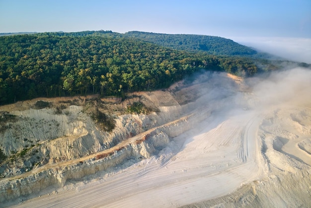 Vue aérienne de l'exploitation minière à ciel ouvert de matériaux calcaires pour l'industrie de la construction avec des excavatrices et des camions à benne basculante