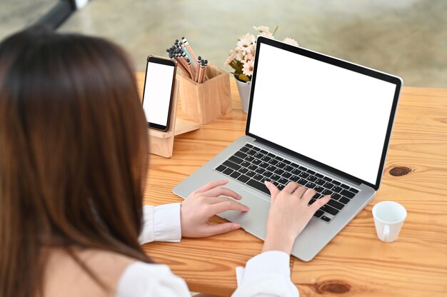 Vue aérienne d'une femme travaillant avec un ordinateur portable et un smartphone sur un bureau en bois.